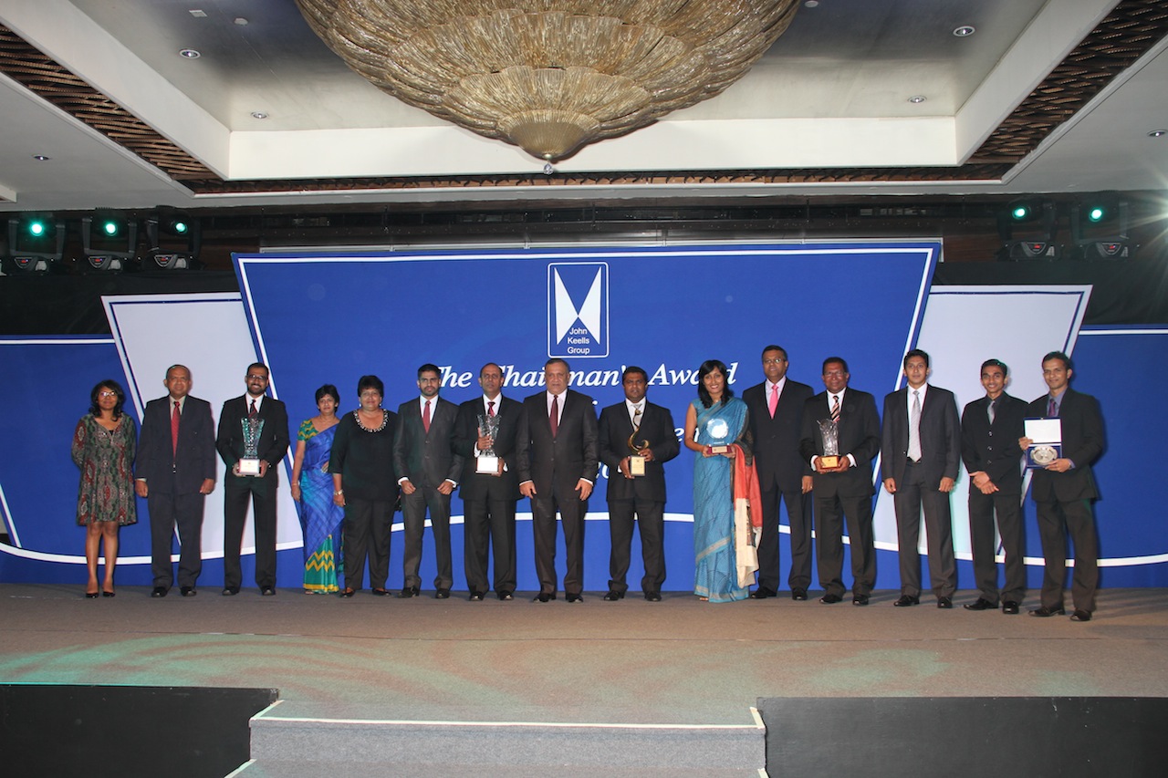 A group of individuals standing in front of a large backdrop displaying The Chairmans Award. They are all dressed in formal attire, holding various awards.